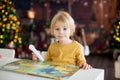 Blond child, toddler boy, having fun at home on Christmas, reading a special book with reader and making quiz Royalty Free Stock Photo