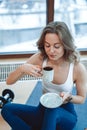 Blond confident girl smiles and enjoys morning coffee in apartment.