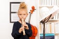 Blond curly girl plays flute standing near cello