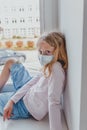 Blond European schoolgirl in quarantine is sad in a mask against coronovirus, wants to walk