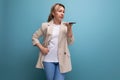 blond european young woman in a jacket dialing an audio message on the phone on a studio background Royalty Free Stock Photo