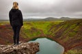 Blond female explorer standing on rock looking at Kerid Crater Lake