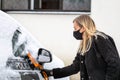 Blond female in face mask with a squeegee cleans snow from a police car