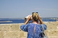 Blond female tourist looks through binoculars at the sea from Gallipoli castle. Apulia, Italy