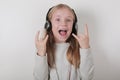 Blond girl with headphones listening music and singing. Cute little girl making a rock-n-roll sign. Royalty Free Stock Photo