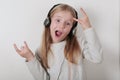 Blond girl with headphones listening music and singing. Cute little girl making a rock-n-roll sign. Royalty Free Stock Photo