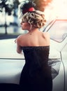 Blond girl model with bright makeup and curly hairstyle in retro style posing near old white car Royalty Free Stock Photo