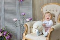 Blond girl posing with husky puppy white color in retro studio shoot with royal armchair. Cute young child play with puppy dogs in