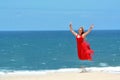 Blond girl with red dress jumping on beach Royalty Free Stock Photo