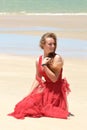 Blond girl with red dress sitting on beach Royalty Free Stock Photo