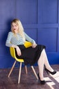 Blond girl in skirt and vest sits on a chair