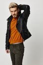 a blond guy in a leather jacket holding his hands behind his head and an orange sweater pants Copy Space Royalty Free Stock Photo