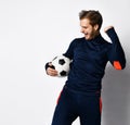 Blond guy, professional soccer player in blue tracksuit is looking overjoyed and holding ball, posing isolated on white. Close up