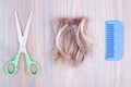 Blond hair lock, metal scissors, plastic comb light wooden background close up, cut off blonde hair curl on bright wood, shears Royalty Free Stock Photo