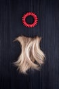 Blond hair lock, red scrunchie black wooden background close up, cut off blonde curl on dark wood, spiral scrunchie, hair band