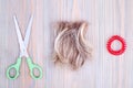 Blond hair lock, scissors, scrunchie light wooden background close up, cut off blonde hair curl on bright wood, shears, hair band