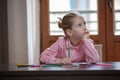 Blond hair school girl boring and tired looking up, sitting at the desk with school supplies, holding her hand over the cheek Royalty Free Stock Photo