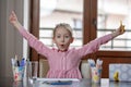 Blond hair school girl, sitting at the desk with school supplies and with her hands raised up Royalty Free Stock Photo