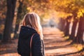 Blond hair woman wearing black coat with hood and looking at alley in autumn park