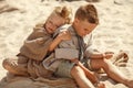 Blond haired brother and sister in cozy knit earth toned clothes playing with sand and showing true emotions Royalty Free Stock Photo