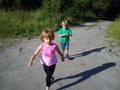 Blond-haired children walk on a dirt road in the summer. Boy in a green T-shirt. Girl in a pink blouse with frill. Brother and Royalty Free Stock Photo