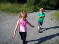 Blond-haired children walk on a dirt road in the summer. Boy in a green T-shirt. Girl in a pink blouse with frill. Brother and Royalty Free Stock Photo