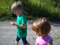 Blond-haired children walk on a dirt road in the summer. Boy in a green T-shirt. Girl in a pink blouse with frill. Brother and Royalty Free Stock Photo