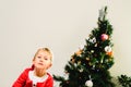 Blond and handsome 5 year old boy dressed up as santa claus next to christmas tree and white background with space for text Royalty Free Stock Photo