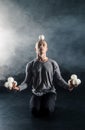 Blond juggler sitting on the floor with white balls on black background