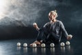 Blond juggler sitting on the floor with white balls on black background