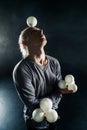 Blond juggler with white balls on black background