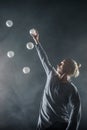 Blond juggler with white balls on black background