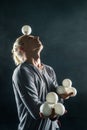 Blond juggler with white balls on black background