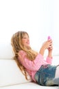 Blond kid girl playing fun with mobile phone on white sofa