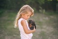 Blond kid girl with puppy pet dog in hands outdoors. Side view Royalty Free Stock Photo