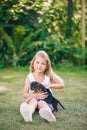 Blond kid girl in white dress with puppy pet dog sit in outdoor green grass Royalty Free Stock Photo