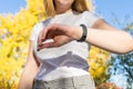 Blond lady looking the screen of the smart watch with autumn leaves on the background. Unrecognizable woman checking and reading