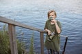 Blond little boy drinking hot tea from thermos isolated over river, male child spending time in open air, wearing green t shirt, Royalty Free Stock Photo