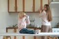 Blond little girl drinking from a large mug. Mom looks after the baby in the kitchen