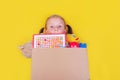 Blond little girl holding a box with toys on yellow background. Donation concept.. Royalty Free Stock Photo