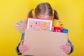 Blond little girl holding a box with toys on yellow background. Donation concept.. Royalty Free Stock Photo