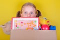 Blond little girl holding a box with toys on yellow background. Donation concept.. Royalty Free Stock Photo