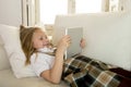 Blond little girl lying on home sofa couch using internet app on digital tablet pad on digital tablet pad Royalty Free Stock Photo