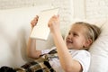 Blond little girl lying on home sofa couch using internet app on digital tablet pad on digital tablet pad Royalty Free Stock Photo