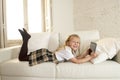 Blond little girl lying on home sofa couch using internet app on digital tablet pad on digital tablet pad Royalty Free Stock Photo
