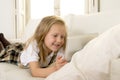 Blond little girl lying on home sofa couch using internet app on digital tablet pad on digital tablet pad Royalty Free Stock Photo