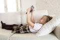 Blond little girl lying on home sofa couch using internet app on digital tablet pad on digital tablet pad Royalty Free Stock Photo