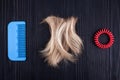 Blond lock of hair, red scrunchie, blue plastic comb black wooden background closeup, cut off blonde hair curl on dark wood, hair Royalty Free Stock Photo
