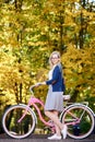 Blond long-haired attractive girl on pink lady bicycle in sunny autumn park on trees background. Royalty Free Stock Photo