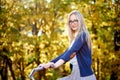 Blond long-haired attractive girl on pink lady bicycle in sunny autumn park on trees background. Royalty Free Stock Photo